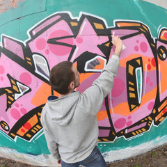 A young guy in a gray hoodie paints graffiti in pink and green c © mehaniq41