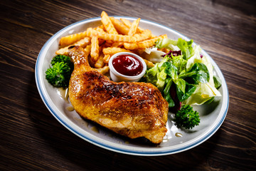 Roasted chicken leg with french fries and vegetable salad on wooden background