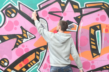 A young guy in a gray hoodie paints graffiti in pink and green c