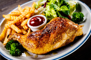 Roasted chicken leg with french fries and vegetable salad on wooden background