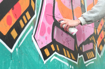 Hand of a young guy in a gray hoodie paints graffiti in pink and