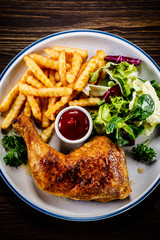 Roasted chicken leg with french fries and vegetable salad on wooden background