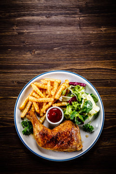 Roasted chicken leg with french fries and vegetable salad on wooden background
