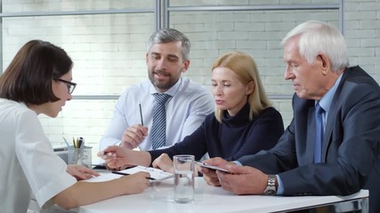 Tracking shot of businessmen and businesswoman giving skills assessment test to young female candidate in glasses during panel job interview