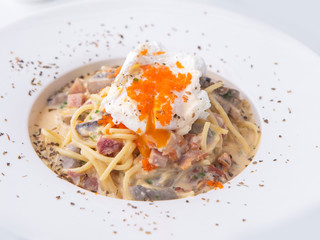 bacon  ham cheese  spaghetti carbonara topped with onsen egg on white plate in restaurant