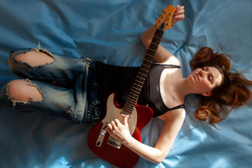 Obraz na płótnie Canvas Girl lying on a blue background with an electric guitar