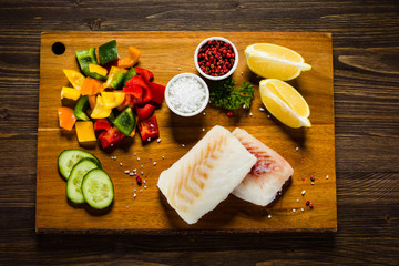 Fresh raw cod with herbs and vegetables served on cutting board on wooden table