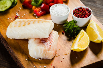Fresh raw cod with herbs and vegetables served on cutting board on wooden table