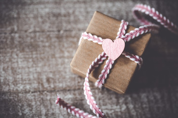 Mit Liebe schenken - Kleines Geschenk mit rosafarbenen Band und Herz auf Holz