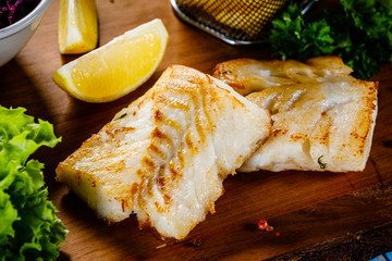 Fish dish - fried fish fillet french fries and vegetables on cutting board on wooden table