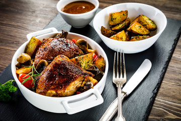 Grilled chicken legs with baked potatoes and vegetable salad on black stone plate