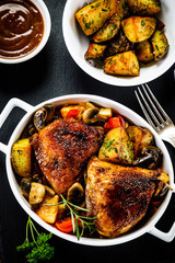 Grilled chicken legs with baked potatoes and vegetable salad on black stone plate