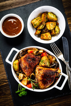 Grilled chicken legs with baked potatoes and vegetable salad on black stone plate