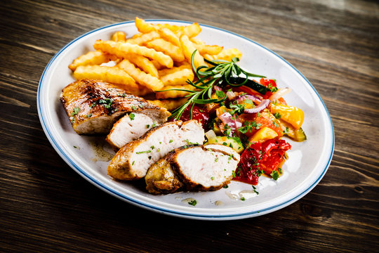 Grilled chicken fillet with french fries on wooden background