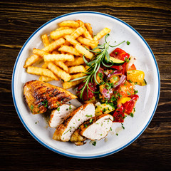 Grilled chicken fillet with french fries on wooden background