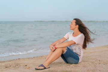 Fototapeta na wymiar Beautiful girl sitting on the beach. Middle aged woman resting at beach near the sea. young, beautiful woman with long flowing hair on the beach.
