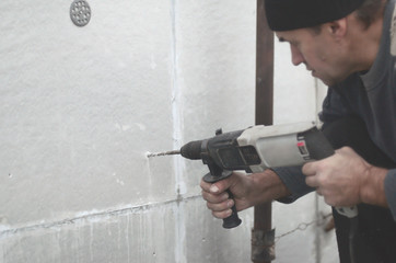 An elderly workman drills a hole in a styrofoam wall for the subsequent installation of a plastic...