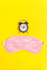 Sleeping eye mask, alarm clock isolated on yellow colourful trendy background. Do not disturb me, let me sleep. Rest, good night, siesta, insomnia, relaxation, tired, travel concept