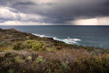 Long exposure shot of oceanside meadow and ocean shore with downpouring storm at London Bridge...