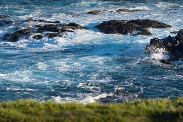 Shot of Ocean-coastal rocky beach and constantly frothing waves with green grassland in the...