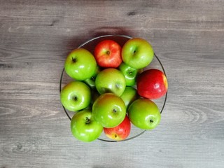 Red and green apple in bowl on wood table.