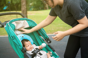 Fototapeta premium Mom walking in park with infant baby boy in stroller