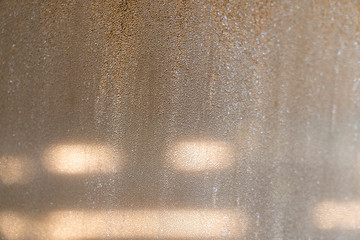 Condensation has happened on the outer surface of the cold window glass with blurry shadow scene of fluorescent light shining outside.