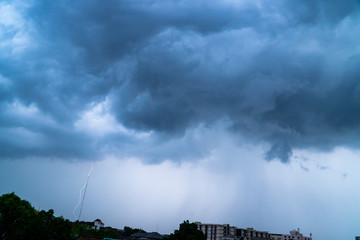Fototapeta premium Dark clouds of a stormy sky background with part of the rain showers in the city and a powerful thunderbolt flashes down to some target on the ground.