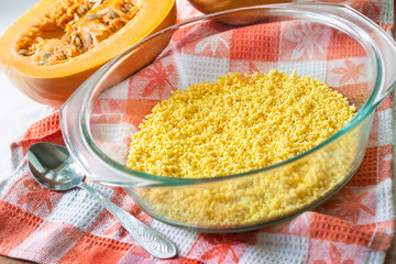 Raw washed millet in a glass pan in the process of cooking sweet milk porridge with pumpkin and raisins