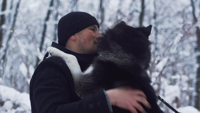 Young man scratches and strokes a beautiful siberian husky best friend in the winter snowy background. Dog and owner on a winter walk in the forest.