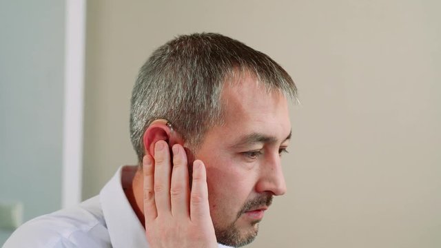 A middle aged man tries on a hearing aid.