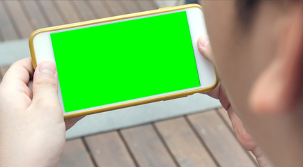 Teen holding a smartphone in the hands of a green screen.