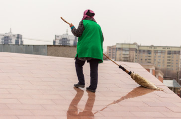 A cleaning lady is sweeping the road with a broom