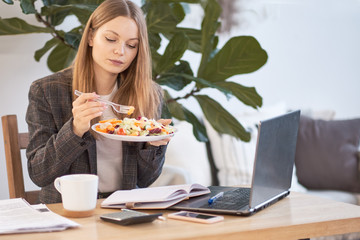 Business woman sitting with a laptop in a cafe and eating breakfast with a cup of coffee on the table.