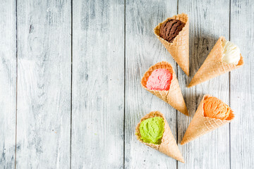 Colorful ice cream in waffle ice cream cones, sweet homemade summer dessert, old wooden background copy space top view