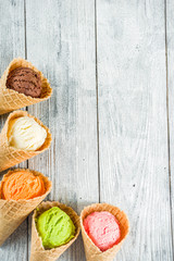 Colorful ice cream in waffle ice cream cones, sweet homemade summer dessert, old wooden background copy space top view