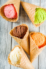 Colorful ice cream in waffle ice cream cones, sweet homemade summer dessert, old wooden background copy space top view