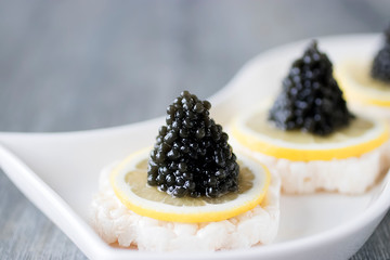 Canapé with black caviar and a slice of lemon on a white plate.