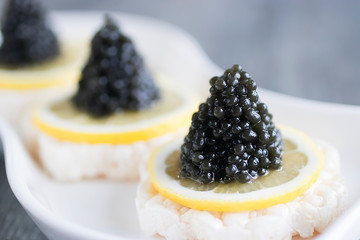 Canape with black caviar and a slice of lemon on a white plate.