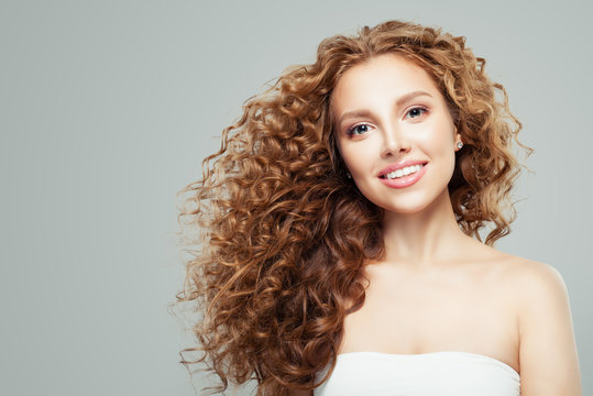Fashion beauty portrait of young redhead woman with long healthy curly hair gray background