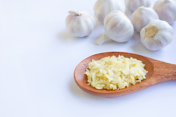 Fresh chopped garlic on wooden spoon with garlic head on white.