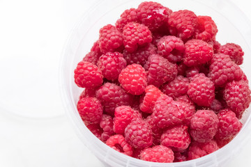 Ripe raspberries in a plastic bucket on a light background