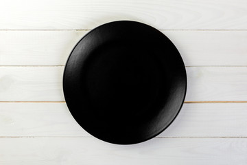 Directy above Empty black matte dish for dinner on white wooden background