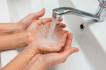 Children's and adult hands take water flowing from the mixer in the palm