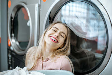 Young and cheerful woman enjoying the washing process standing near professional drying machine in...