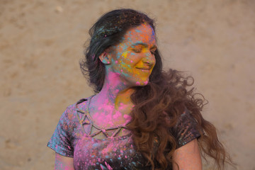 Closeup portrait of pleased brunette girl posing covered with dry Holi paint at the desert