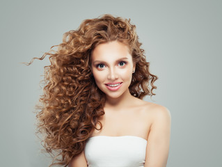 Smiling redhead woman with long healthy curly hair and clear skin. Cute girl on gray background