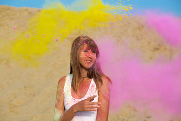 Joyful blonde woman enjoying Holi festival at the desert. Woman posing with exploding dry paint