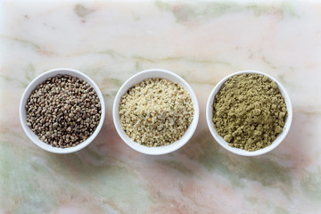 Organic hemp whole seeds, hulled seeds and protein powder in bowls on a marble background