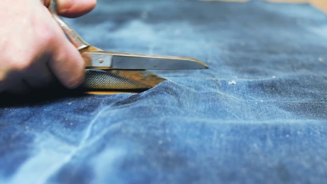Hand of Seamstress cutting a Jeans fabric with scissors on wooden table 